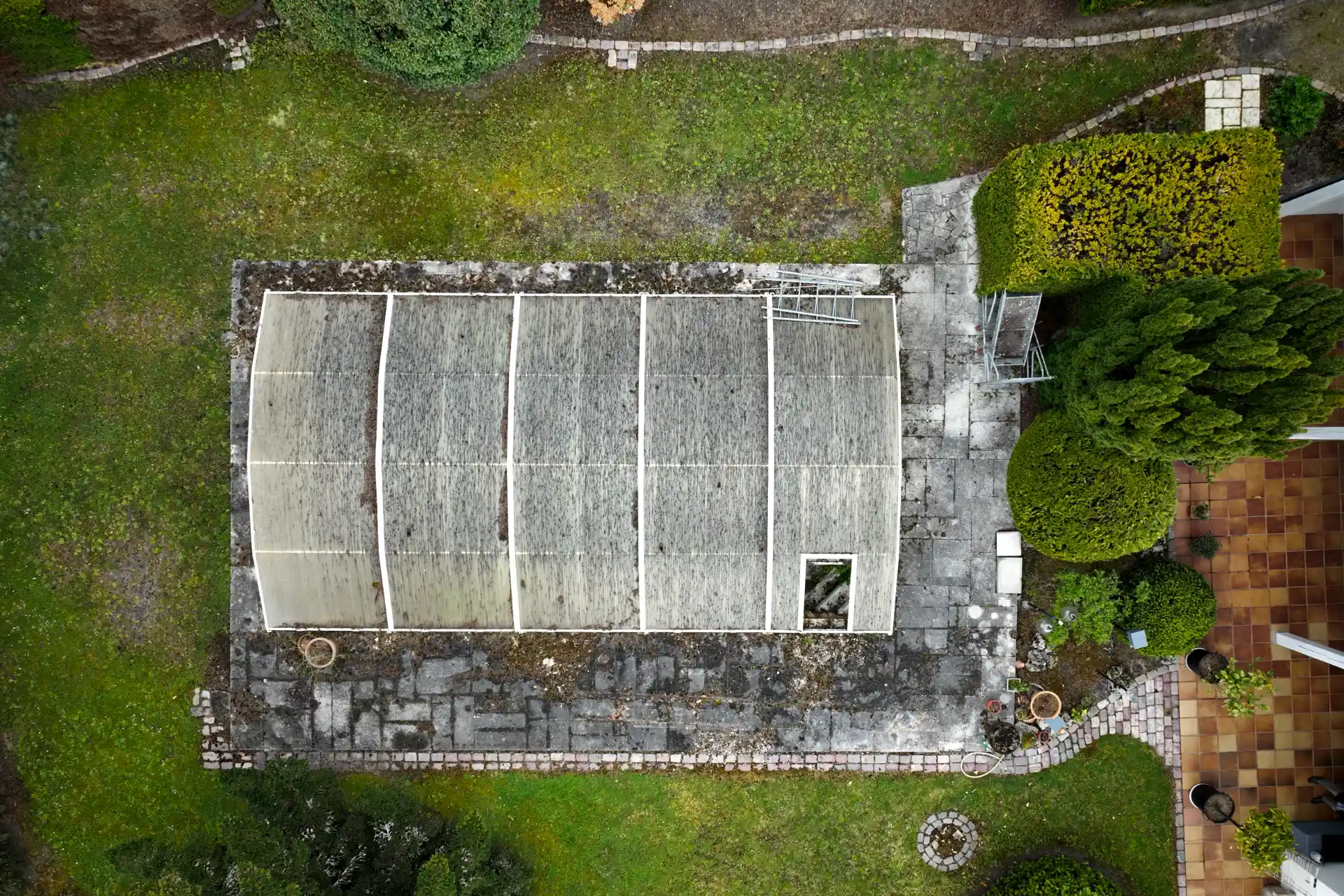 Vue aérienne par drone d’une ancienne structure de piscine couverte, à l’abandon, entourée de jardin
