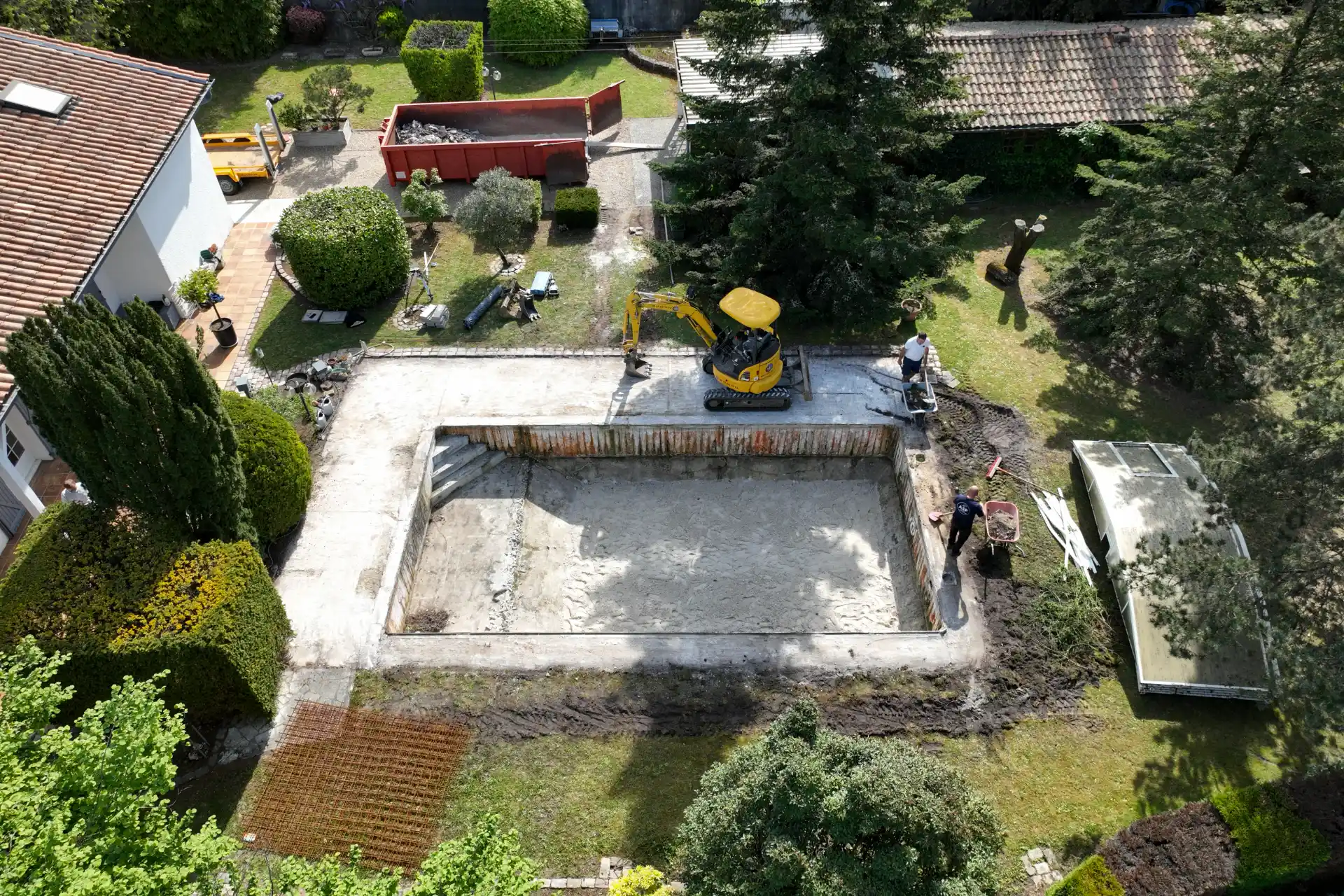 Vue aérienne par drone d’une mini-pelle en train de démolir l’ancien bassin de piscine, benne à gravats sur le côté