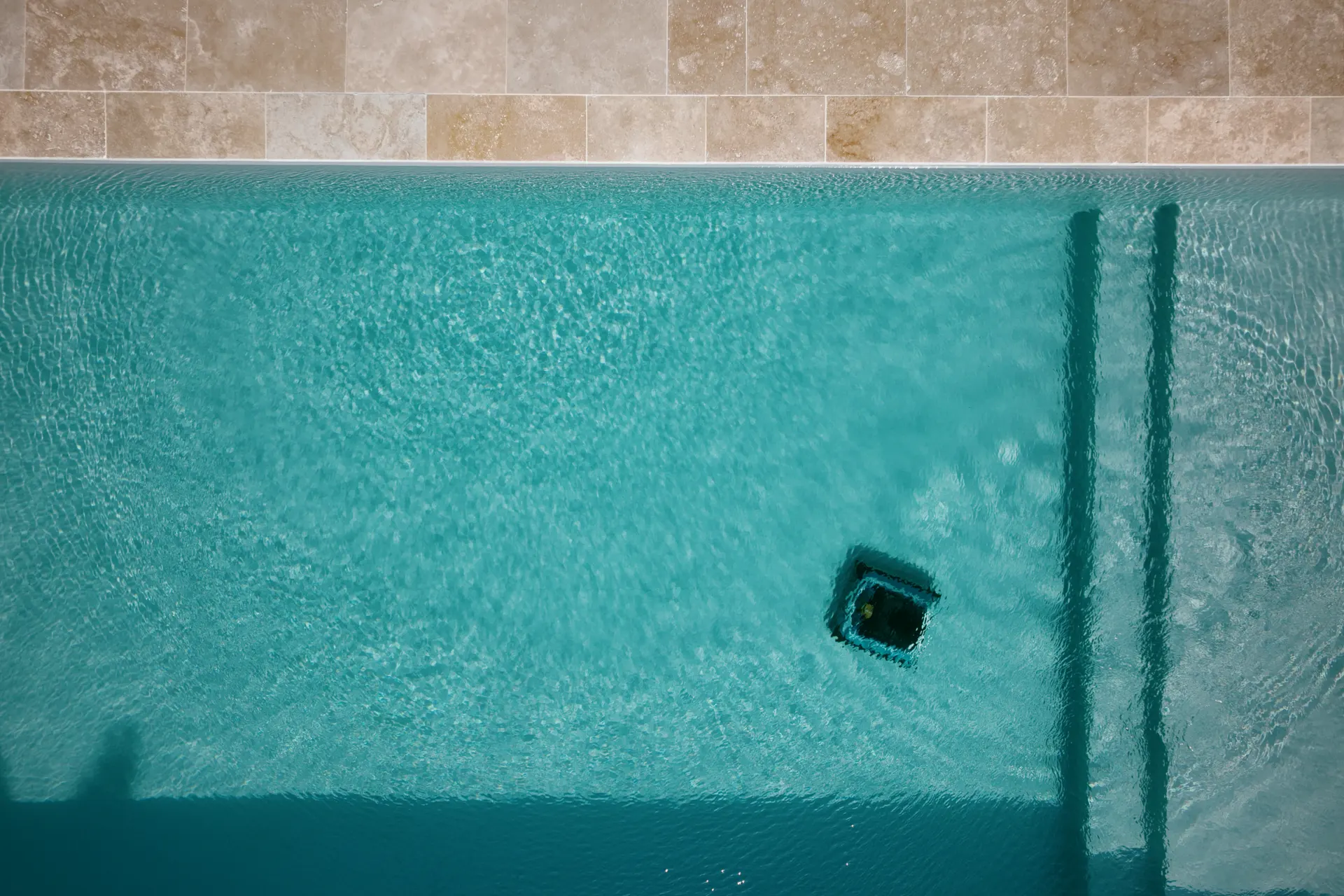 Vue zénithale par drone d’une eau de piscine turquoise et limpide, margelles en pierre posées