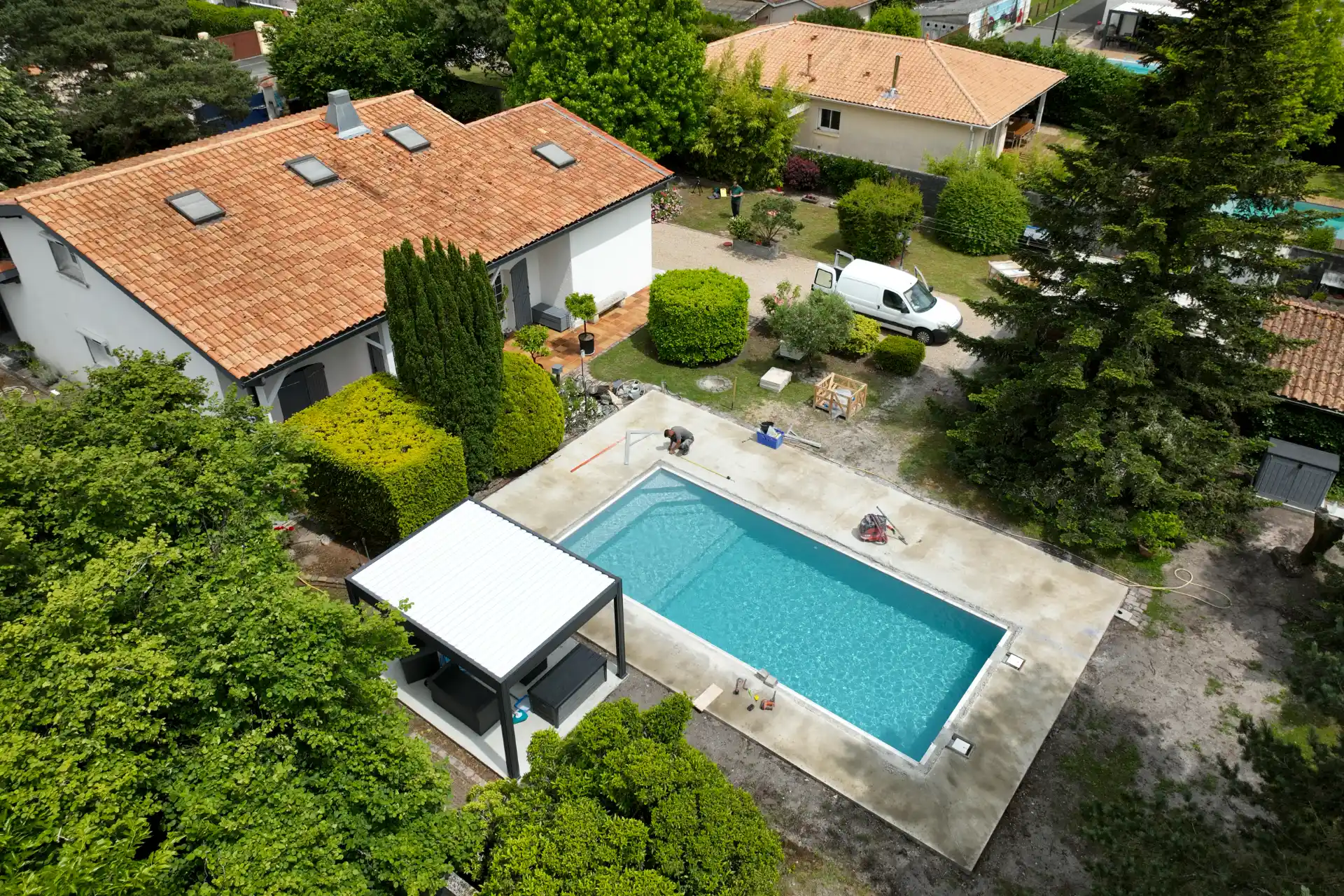 Vue aérienne par drone d’une piscine en phase de finitions, terrasse et véhicule utilitaire du pisciniste sur site