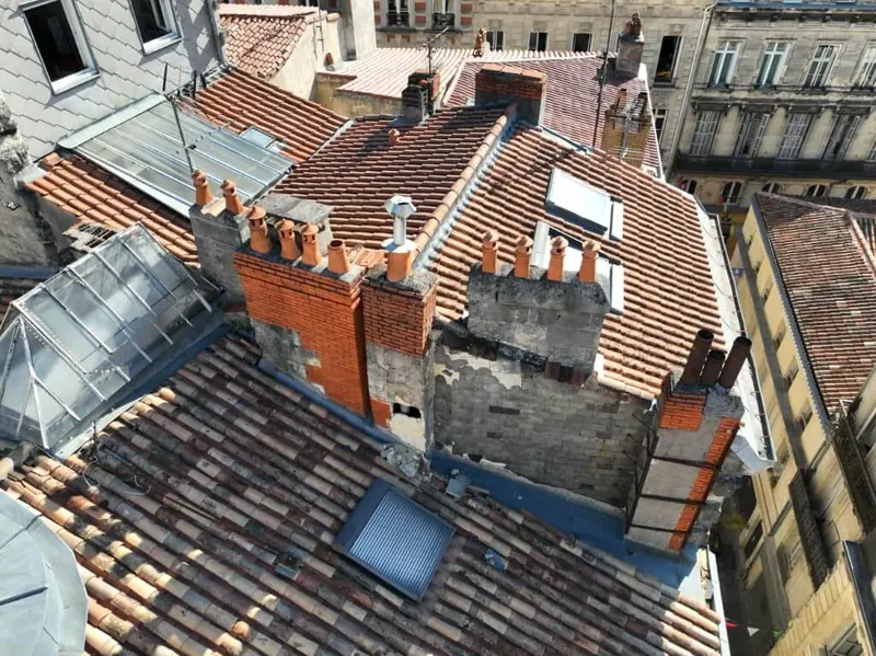 Toitures d’immeubles anciens à Bordeaux vues par drone, avec plusieurs souches de cheminée aux enduits dégradés