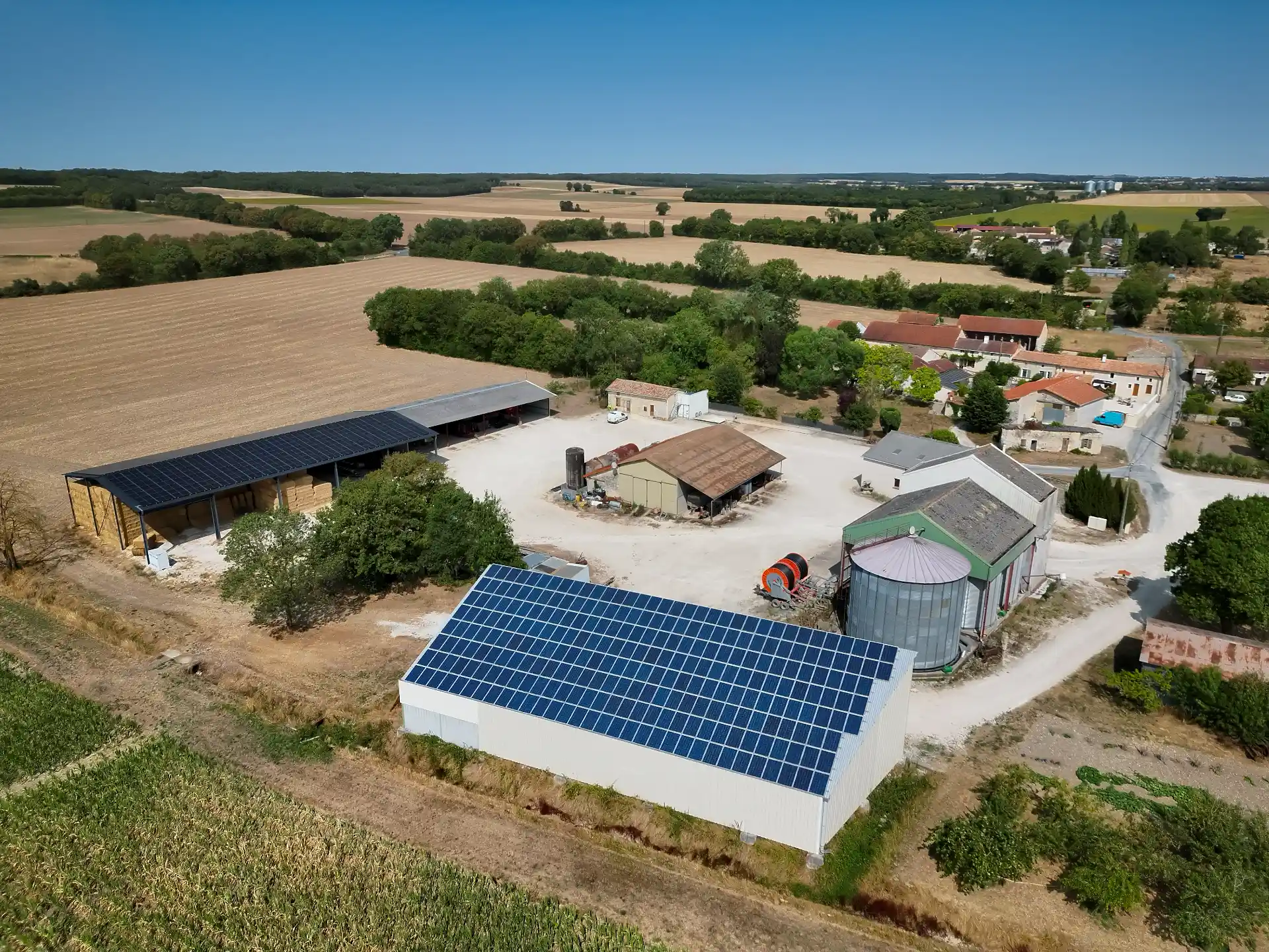 Vue aérienne d’une exploitation agricole avec plusieurs hangars, dont deux toitures couvertes de panneaux photovoltaïques, en Charente